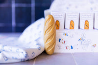 Senteurs De France The "Baguette" Soap by Senteurs De France sits beside its illustrated decorative box on a playful patterned cloth—an ideal French bakery-inspired keepsake.