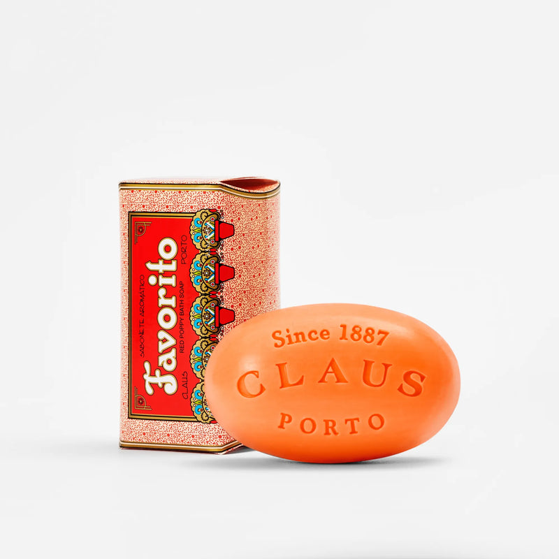 A Claus Porto 1887's Favorito Red Poppy Soap - 150gm bar with embossed lettering next to its red and gold vintage packaging, isolated on a white background.