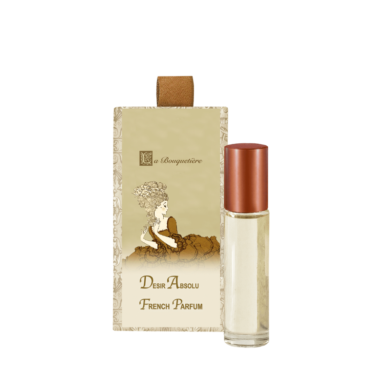 A bottle of La Bouquetiere Desir Absolu French perfume roller next to its packaging, which features elegant vintage-style artwork of a woman sitting on a cloud.