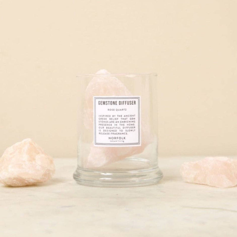 The Norfolk Natural Living Rose Quartz Gemstone Diffuser, a clear glass container with pale pink rose quartz inside and beside it, adds emotional healing and aromatherapy to your space.