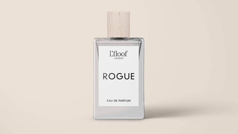 A minimalist perfume bottle featuring a wooden cap and a white label. The label displays "L'floof LONDON" at the top and showcases "ROGUE" prominently in bold letters across the middle, capturing the essence of L'floof ROGUE Dog Perfume Fragrance Spray. At the bottom, it reads "EAU DE PARFUM." The background is a plain beige color.