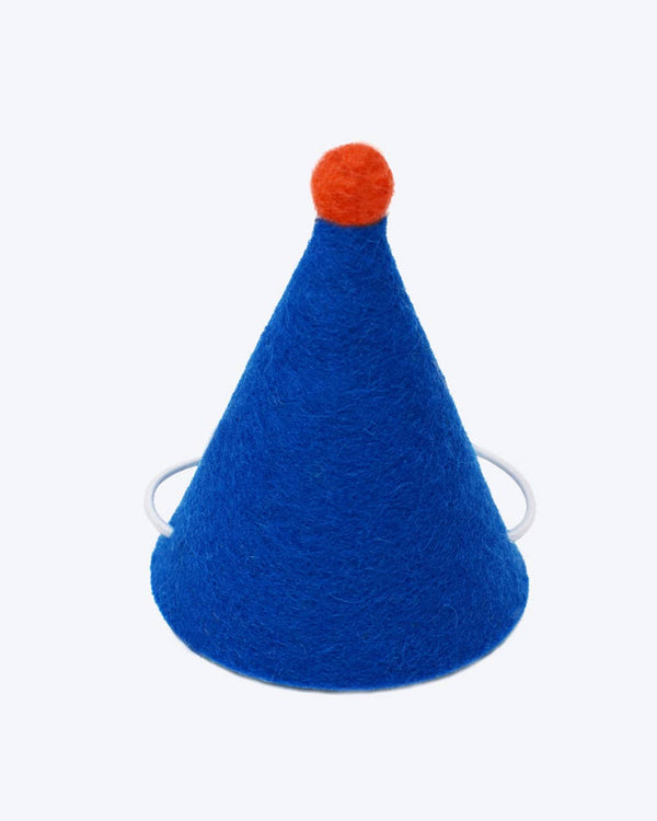 The MODERNBEAST Wool Pet PAWTY HAT features blue wool, a round red pom-pom top, and an elastic strap for wearing, shown against a plain white background.