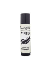 A tube of Stewart & Claire Winter Lip Balm with Cinnamon features a cinnamon stick illustration and "scented with cinnamon" text on a white background. This moisturizing balm has a black cap.