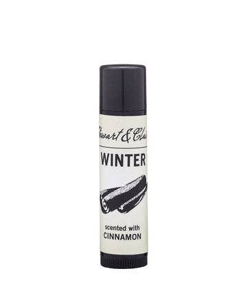 A tube of Stewart & Claire Winter Lip Balm with Cinnamon features a cinnamon stick illustration and "scented with cinnamon" text on a white background. This moisturizing balm has a black cap.