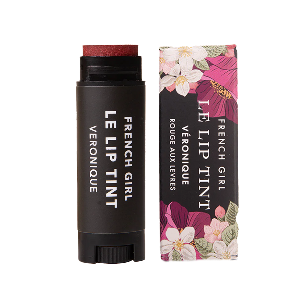 A tube of FRENCH GIRL Tinted Lip Balm in Veronique, a reddish shade, is placed beside its floral-patterned box. Both the tube and packaging feature the FRENCH GIRL product name in white lettering.