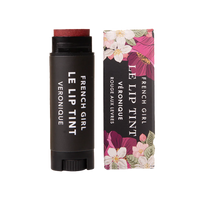 A tube of FRENCH GIRL Tinted Lip Balm in Veronique, a reddish shade, is placed beside its floral-patterned box. Both the tube and packaging feature the FRENCH GIRL product name in white lettering.