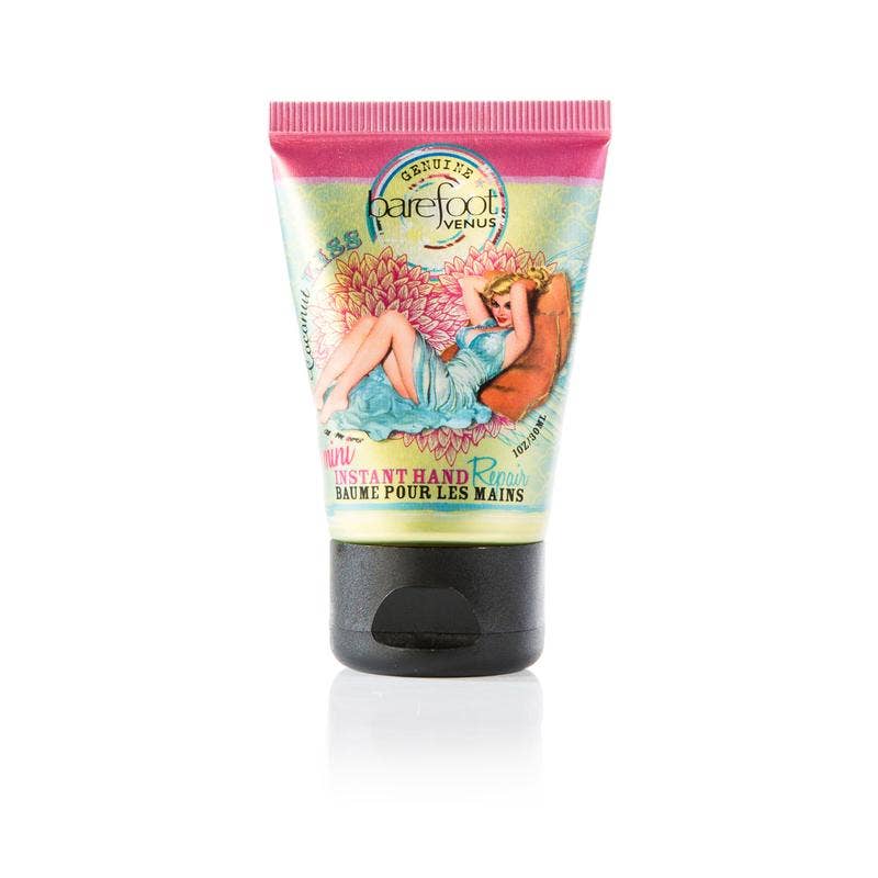 A small, colorful tube of Barefoot Venus Coconut Kiss Mini Hand Repair Balm featuring artwork of a reclining woman surrounded by flowers. The top is pink, and the bottom is black. Infused with an Island Coconut scent, this cruelty-free product has text primarily in English and French.
