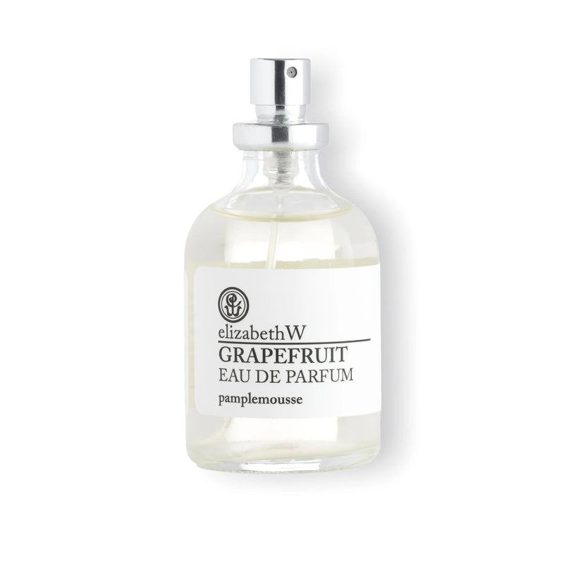 A clear glass bottle of Elizabeth W Purely Essential Grapefruit Eau de Parfum, handcrafted perfume with a spray nozzle, against a white background. The label features black text.