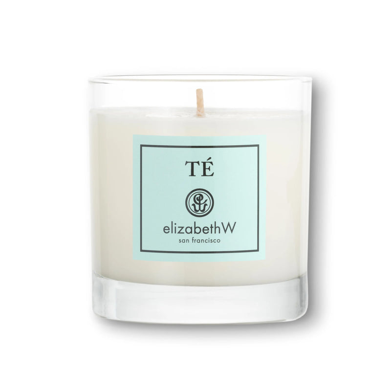 A soy wax candle in a clear glass container, depicting a teal label with the text "té" at the top, a swirl logo, and "elizabeth W San Francisco" on it.