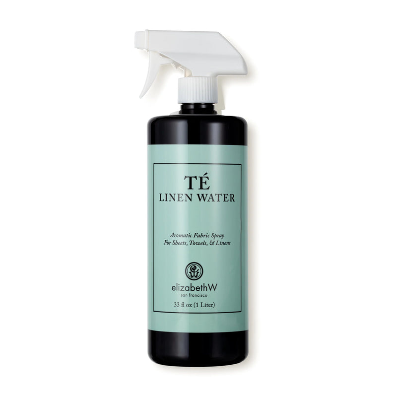 A black spray bottle labeled "elizabeth W Signature Té Linen Water," described as oriental black tea-scented aromatic freshener for sheets, towels, and linens, contains 