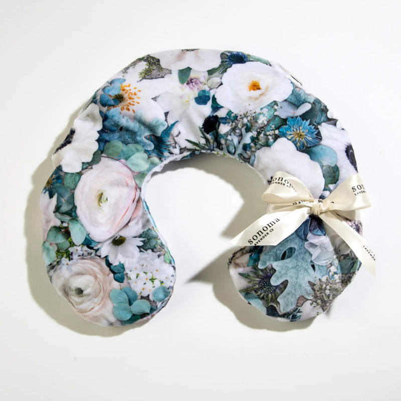 The Sonoma Eucalyptus Blooming Buds Neck Pillow by Sonoma Lavender features a floral design with white, blue, and green blooms, tied with a cream ribbon for aromatic eucalyptus lavender comfort—ideal for soothing relaxation. Placed on a white background.