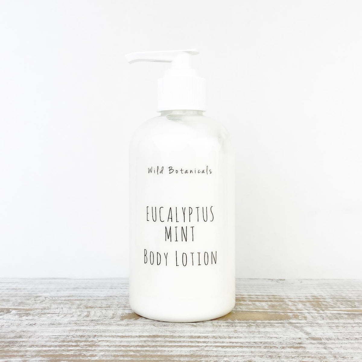 A clear plastic bottle with a pump dispenser labeled "Wild Botanicals Eucalyptus Mint Lotion - 8 oz" against a plain white background with a light wood surface.