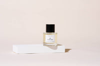 A bottle of Goldie Dog Fragrance - Summer Tonic with a black cap rests on a white platform against a light beige background, showcasing the refined style of Goldie's luxury dog grooming products.