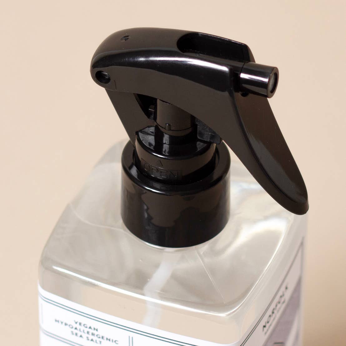 Close-up of the Norfolk Natural Living Rose Garden Scented Vinegar, a clear plastic bottle with a black trigger spray, labeled vegan and hypoallergenic, rose fragrance, by Norfolk Natural Living, set against a plain beige background.