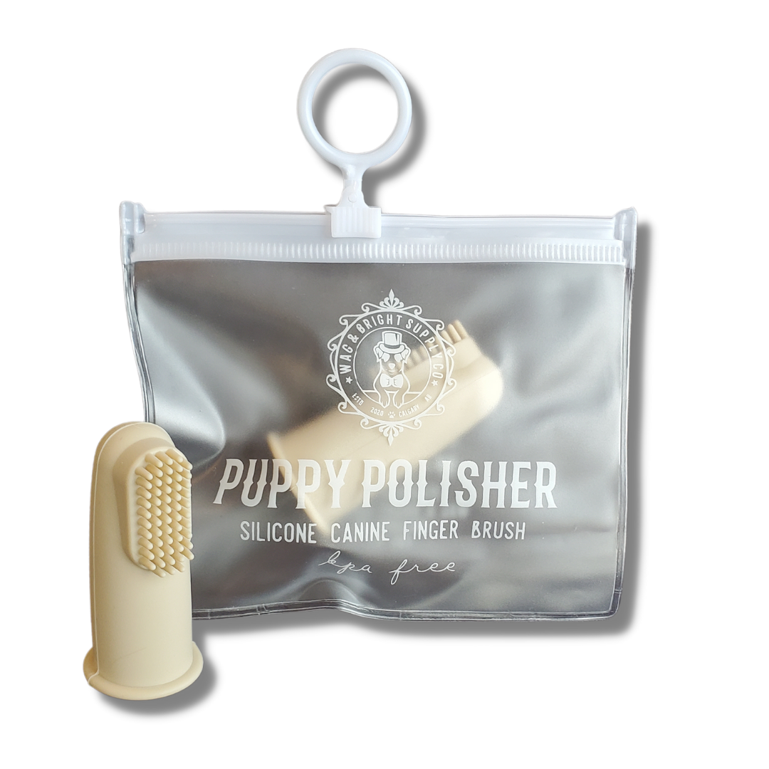 A "Puppy Polisher Finger Brush" from Wag & Bright Supply Co. is displayed next to its transparent zippered pouch. The cream-colored silicone finger brush is designed for pet dental care and features small silicone bristles. The pouch, which displays the brand details, includes a loop handle for added convenience.