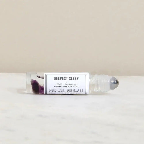 The Norfolk Natural Living Deepest Sleep Pulse Point Oil (10ml) rests on a white surface, featuring clear liquid and amethyst gemstones to support restful sleep.