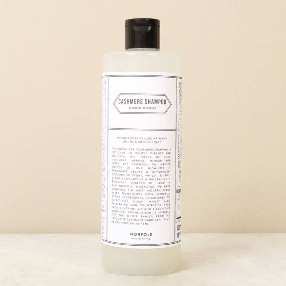 A clear plastic bottle with a black cap labeled "Norfolk Natural Living Cashmere Shampoo" for delicate fiber care, featuring ingredients and natural moth deterrent benefits by Norfolk Natural Living, shown on a neutral surface.