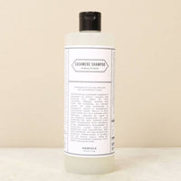 A clear plastic bottle with a black cap labeled "Norfolk Natural Living Cashmere Shampoo" for delicate fiber care, featuring ingredients and natural moth deterrent benefits by Norfolk Natural Living, shown on a neutral surface.