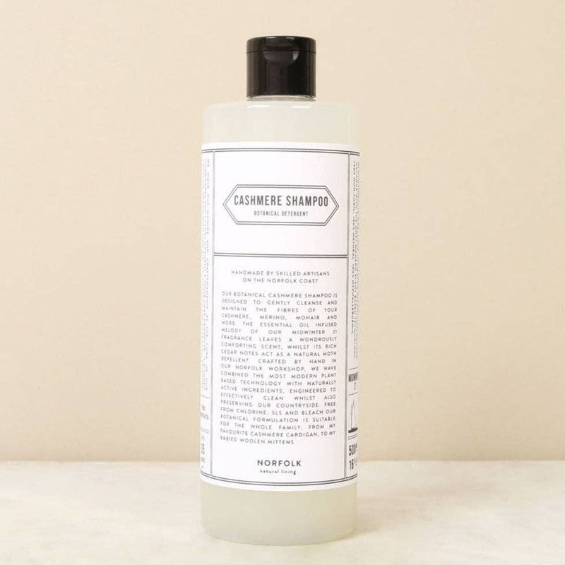 A clear plastic bottle with a black cap labeled "Norfolk Natural Living Cashmere Shampoo" for delicate fiber care, featuring ingredients and natural moth deterrent benefits by Norfolk Natural Living, shown on a neutral surface.