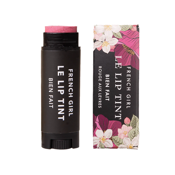 A tube of FRENCH GIRL Tinted Lip Balm | Bien Fait, in a sleek black container with white text, sits next to its floral-patterned box decorated with pink, white, and green flowers accented by gold.