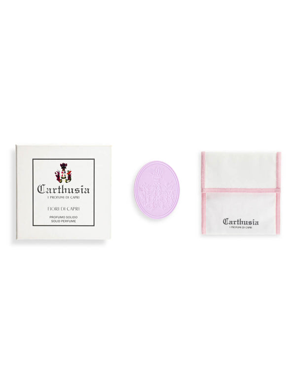 A white Carthusia I Profumi di Capri Fiori di Capri Solid Perfume box, a round lavender solid perfume, and a white cloth with pink trim and logo are elegantly arranged on a white background to evoke luxury fragrance.