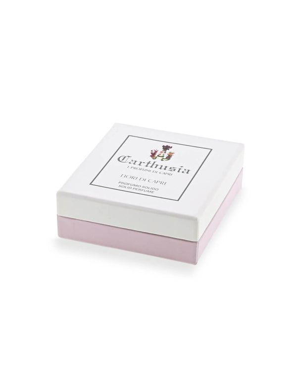 A square white and pale pink box with the Carthusia I Profumi di Capri label and floral emblem holds the Carthusia Fiori di Capri Solid Perfume, elegantly photographed against a white background.