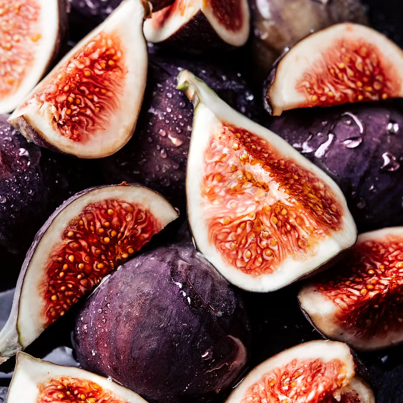 Close-up of fresh figs, whole and halved, display their vibrant insides and glistening deep purple skins—capturing the essence of ISULA parfums Fiori di Ficu - Fig Blossom eaux de toilette by ISULA parfums.