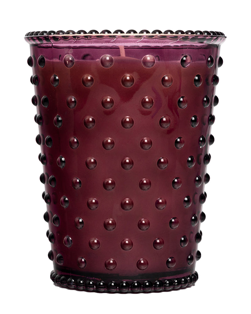 The Simpatico No. 98 Fig Hobnail Glass Candle by Simpatico features a purple glass holder with a hobnail texture and is filled with natural soy wax scented with fig.