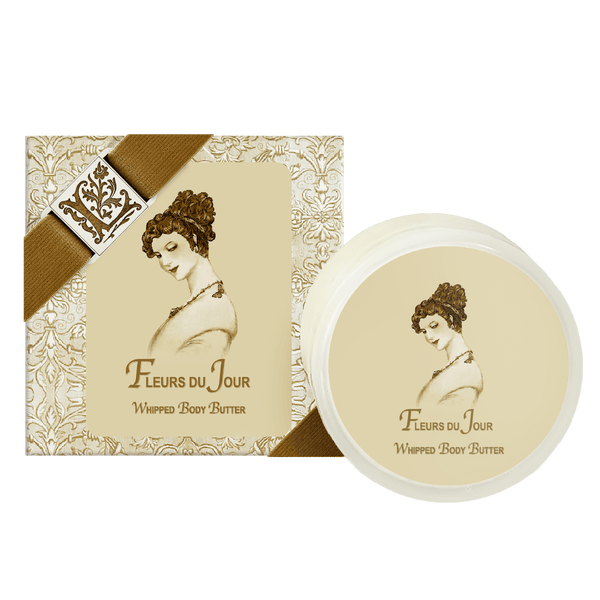 A display features La Bouquetiere Fleurs du Jour / Marina Blue Argan Oil Whipped Body Butter, highlighted with vintage-style packaging showing a curly-haired woman and decorated with a pattern and brown ribbon.