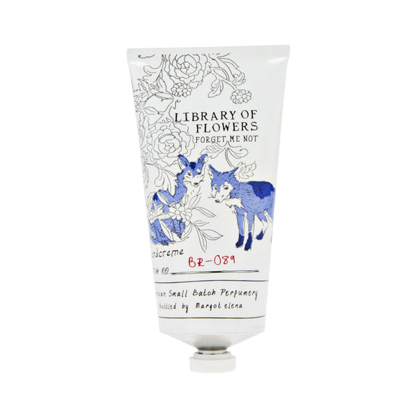A white tube of Margot Elena Library of Flowers Forget Me Not Hand Creme displays floral art and two blue foxes, with the label highlighting shea butter, handwritten-style accents, and a batch number.