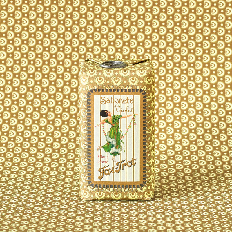 The Claus Porto 1887 Classico Fox Trot Violet Soap, wrapped in gold patterned paper with a dancing woman illustration, offers a classic violet scent and floral fragrance.