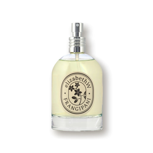 A bottle of elizabeth W Botanist's Scent Lab Frangipani Eau de Parfum is displayed against a white background. The clear bottle with a silver spray cap contains a light yellow liquid. Its label, adorned with the elizabeth W brand name and a floral design, hints at notes of sandalwood and orange blossom within.