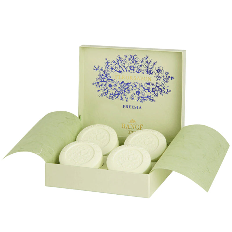 The unwrapped box of Rancé Classic Soap - Freesia by Rancé showcases four round, embossed 3.5 oz spring floral soaps. The box features a delicate blue floral pattern on the lid and is enveloped in a soft light green shade, encapsulating the essence of fresh blooms in each soap.