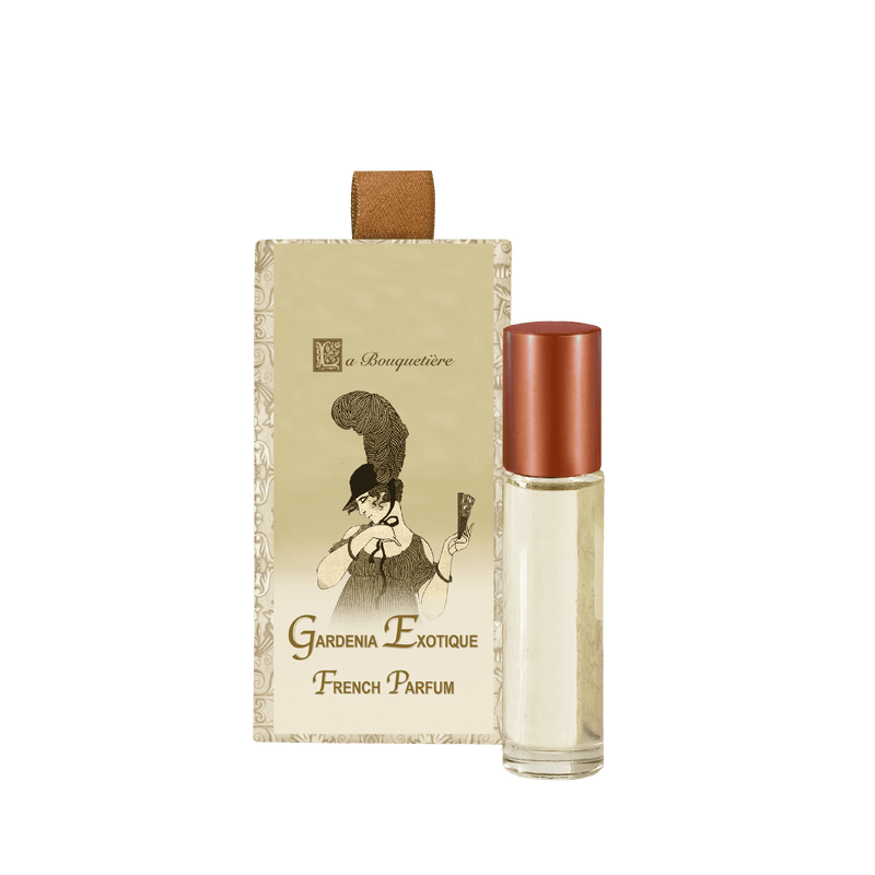A La Bouquetiere Gardenia Exotique Perfume Roller stands next to its ornate packaging. The packaging features an illustration of a person in vintage attire holding a trumpet. The perfume roller has a copper-colored cap and contains a light-colored liquid, with gardenia and orange blossom notes.