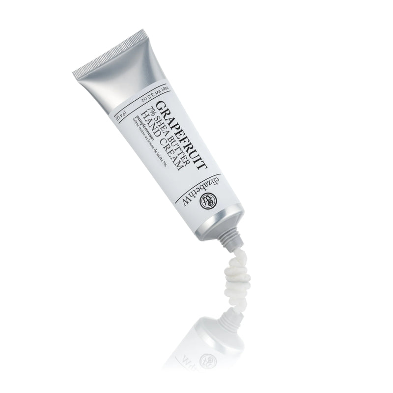 A tube of elizabeth W Purely Essential Grapefruit Hand Cream squeezed partially on a reflective white surface, with the hydrating cream forming a small peak at the tube's opening.
