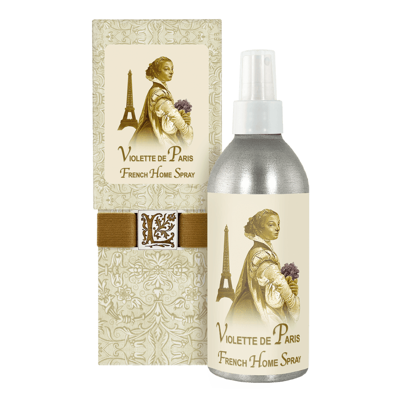A bottle of La Bouquetiere Violette de Paris Home Spray next to its packaging. The packaging features an elegant vintage design with an illustration of a woman holding flowers near the Eiffel Tower.