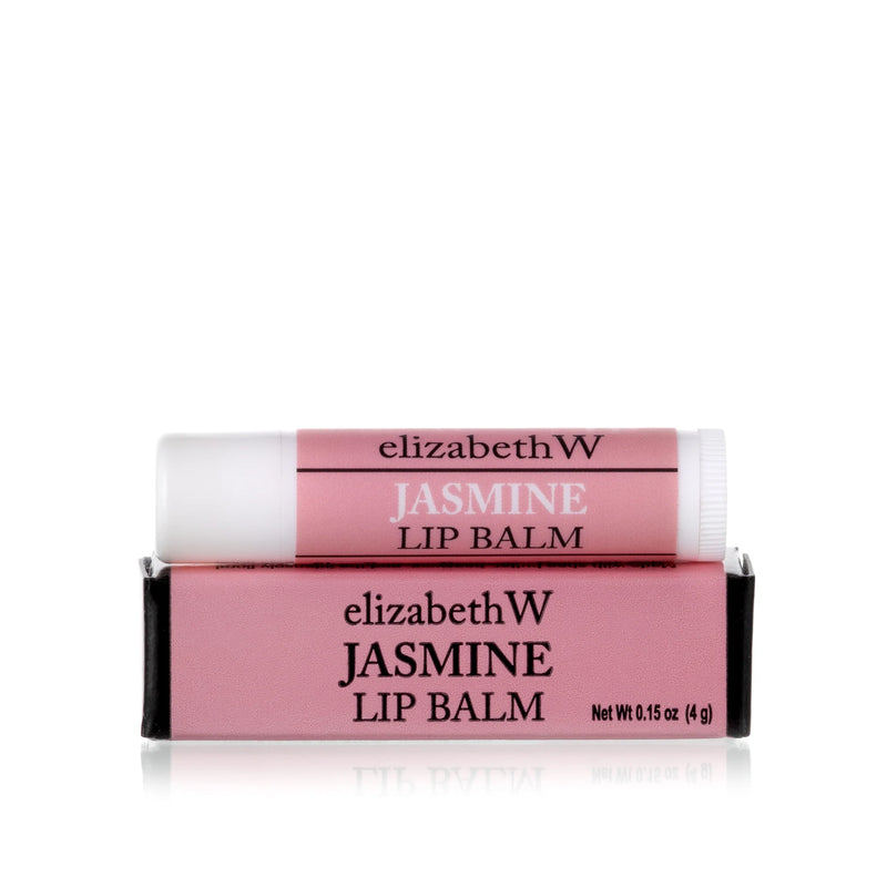 Two tubes of elizabeth W Botanical Apothecary Jasmine Lip Balm with shea butter, one placed on top of the other in a pink and white box, on a reflective white surface.