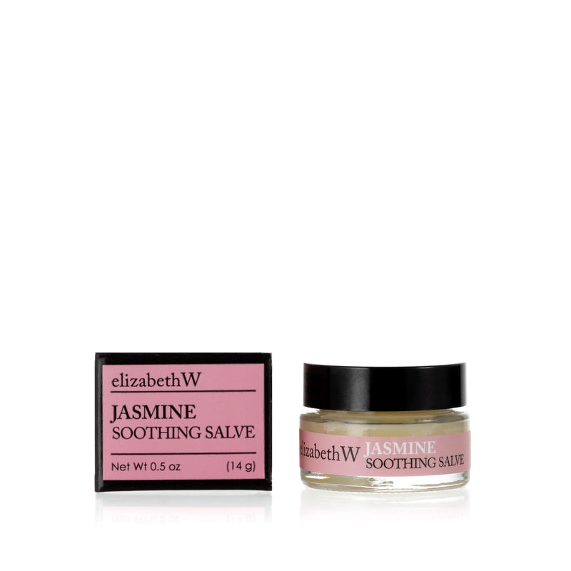 A small glass jar of elizabeth W Botanical Apothecary Jasmine Soothing Salve for dry skin next to its packaging box on a white background. The box and jar labels are pink with white text.