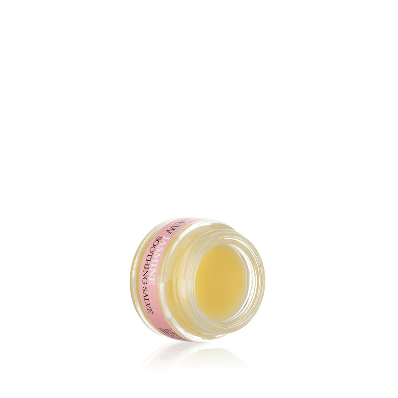 A small, open jar of yellow elizabeth W Botanical Apothecary Jasmine Soothing Salve with a pink label on a reflective white surface, isolated on a white background.