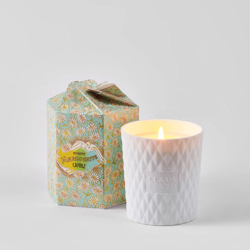 A lit Claus Porto 1887 Ltd Edition Marguerite Jasmine Breeze Candle in a textured holder sits beside its floral-patterned box, highlighting Portuguese craftsmanship, on a light gray background.