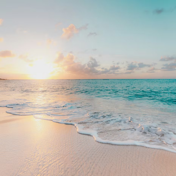 A golden sunrise over calm ocean waves and a pastel sky captures the serene essence of ISULA parfums Fiore di l’Arinella - Beach Flower eaux de toilette.