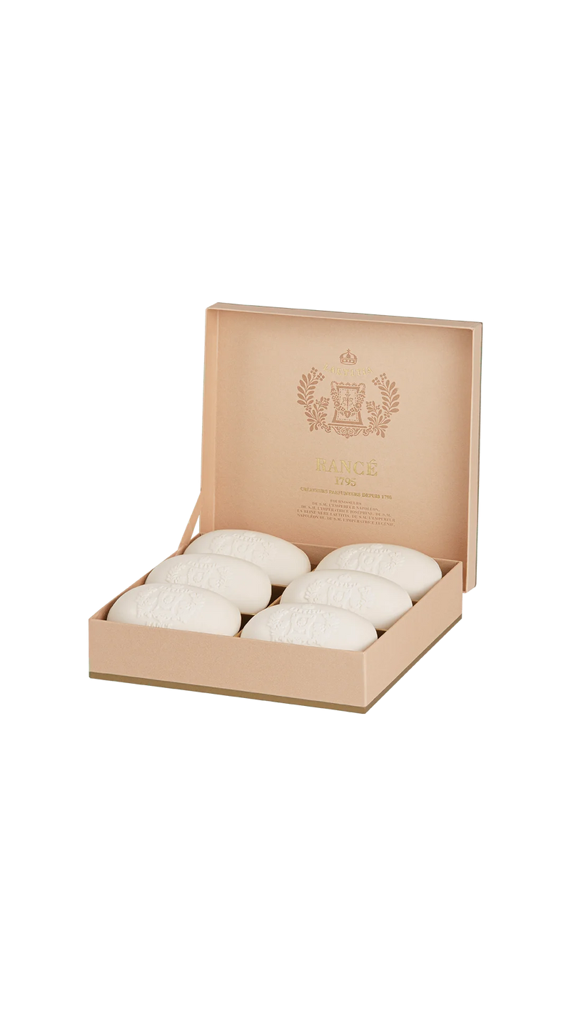 The Rancé Laetitia Luxury Soap Box features six oval, embossed white soaps arranged in two rows within an open beige box. The propped lid displays a decorative "Rancé 1795" logo against a plain green background, exuding timeless charm and elegance.