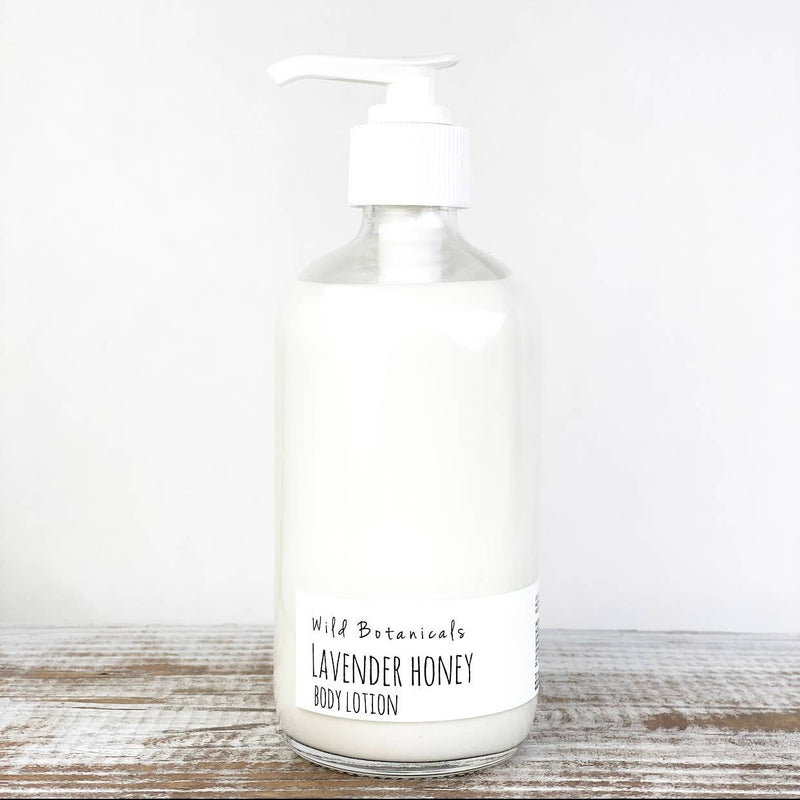 A glass pump bottle of Wild Botanicals Lavender Honey BodyLotion is centered against a plain white background. The bottle contains a creamy smooth lotion made with lavender and fresh honey, and it has a simple white label with the product name printed in black text.