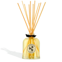 The elizabeth W Botanist's Scent Lab Leaves Diffuser features a clear glass bottle with yellow liquid, wooden reed sticks, a round label, and a black bow, filling your space with a fresh green leafy fragrance.