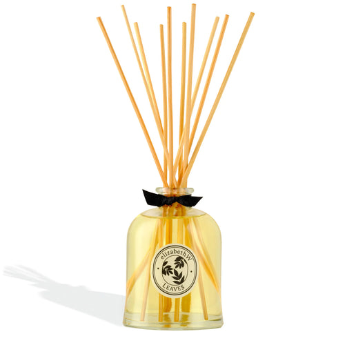 The elizabeth W Botanist's Scent Lab Leaves Diffuser features a clear glass bottle with yellow liquid, wooden reed sticks, a round label, and a black bow, filling your space with a fresh green leafy fragrance.