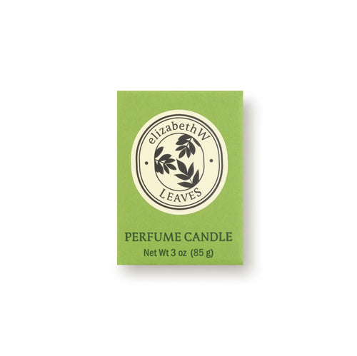 A green box labeled "elizabeth W" shows a round black leaf logo. Below: "Botanist's Scent Lab Leaves Votive Candle, Net Wt 3 oz (85 g)," a soy wax candle with Atlas cedar and sandalwood notes, sits on a plain white background.