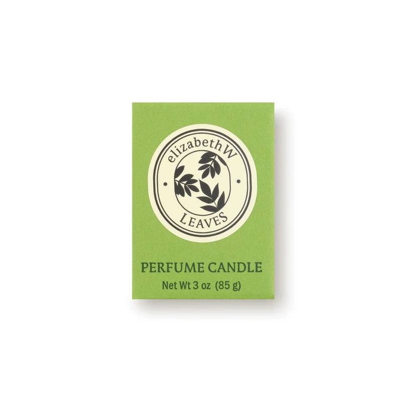 A green box labeled "elizabeth W" shows a round black leaf logo. Below: "Botanist's Scent Lab Leaves Votive Candle, Net Wt 3 oz (85 g)," a soy wax candle with Atlas cedar and sandalwood notes, sits on a plain white background.