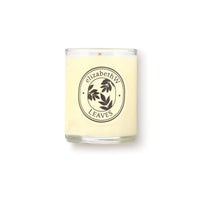 The elizabeth W Botanist's Scent Lab Leaves Votive Candle features a cream-colored soy wax in a clear glass jar with a dark leaf art label. It blends notes of Atlas cedar and sandalwood. The background is plain white.