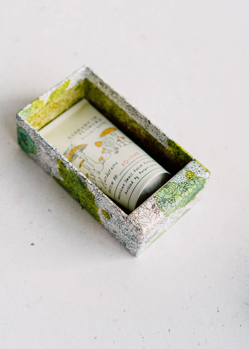 A handmade decorative box with flowering lotus prints containing a tube of Margot Elena's Library of Flowers Willow & Water Hand Creme, placed on a white background. The box has a garden theme with green, yellow, and white colors.