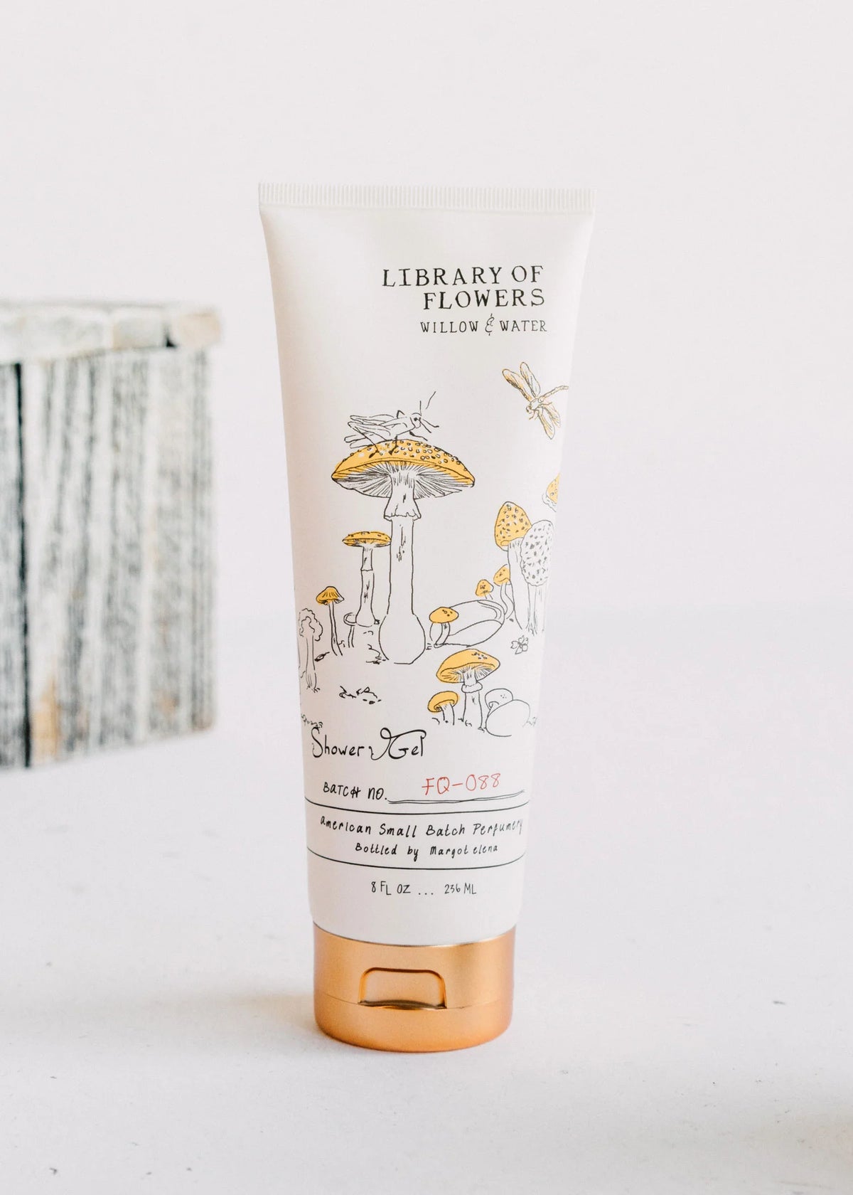 A tube of Margot Elena brand "Library of Flowers Willow & Water" shower gel, featuring whimsical illustrations of mushrooms and plants from the Gardens of Imagination, standing upright against a soft, neutral background.